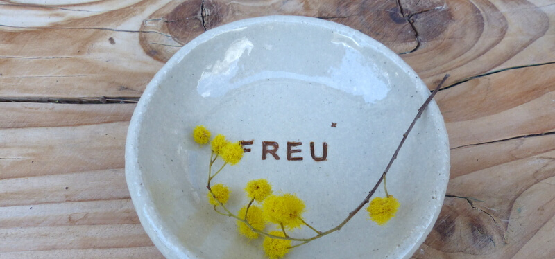 Keramikschälchen mit gestempeltem Schriftzug "FREU", in der Schale liegen gelbe Blüten